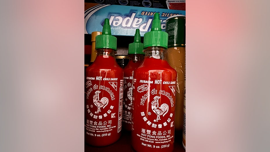 Three Huy Fong sriracha bottles in a pantry.