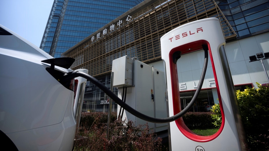 A Tesla charges with Chinese characters on a building in the background