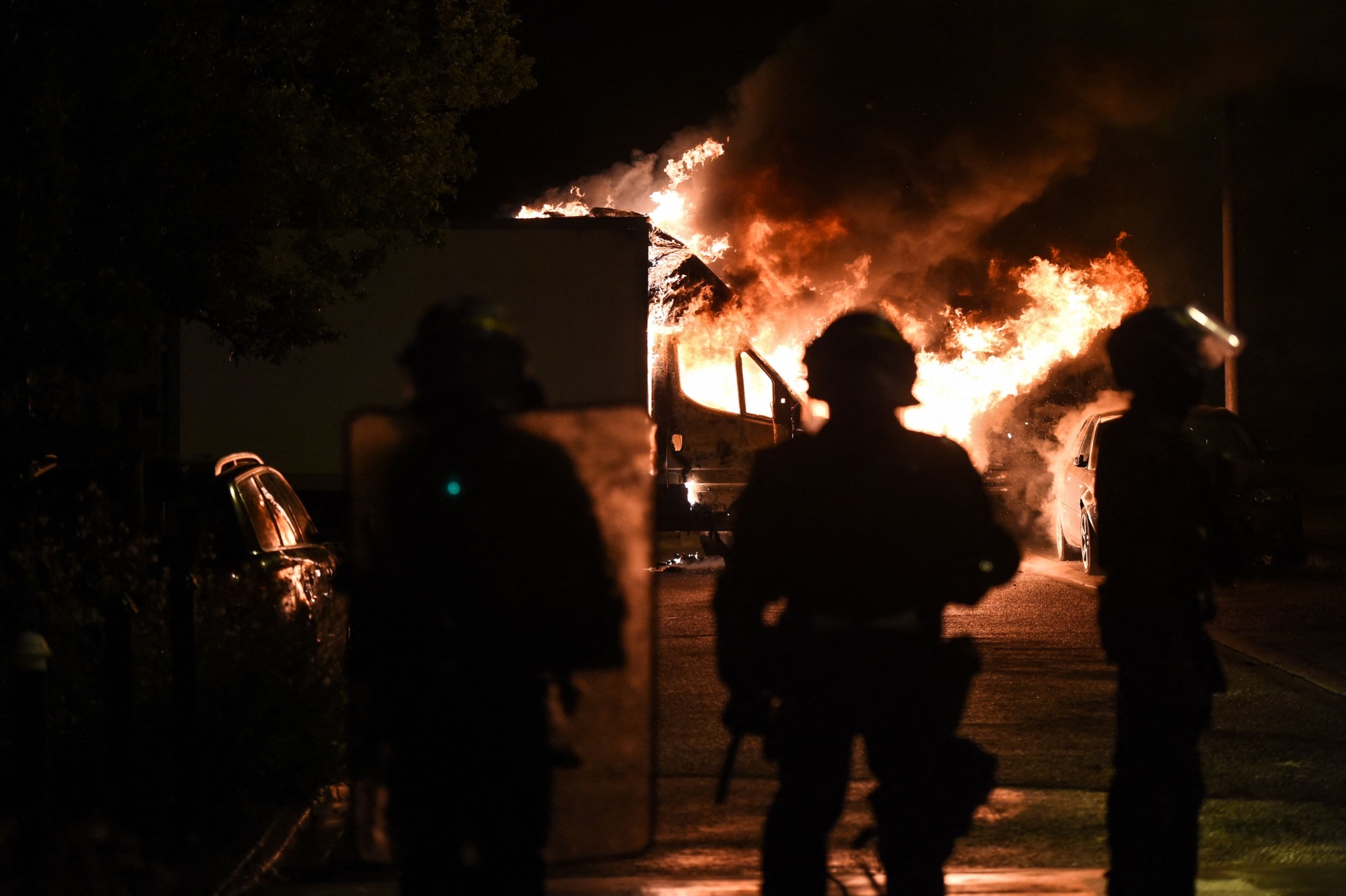 TOPSHOT - French anti riot police officers watch a truck burn in Nantes, western France on early July 1, 2023, four days after a 17-year-old man was killed by police in Nanterre, a western suburb of Paris. French President Emmanuel Macron has announced measures including more police and urged parents to keep minors off the streets as he battled to contain nightly riots over a teenager's fatal shooting by an officer in a traffic stop. (Photo by Sebastien SALOM-GOMIS / AFP) (Photo by SEBASTIEN SALOM-GOMIS/AFP via Getty Images)