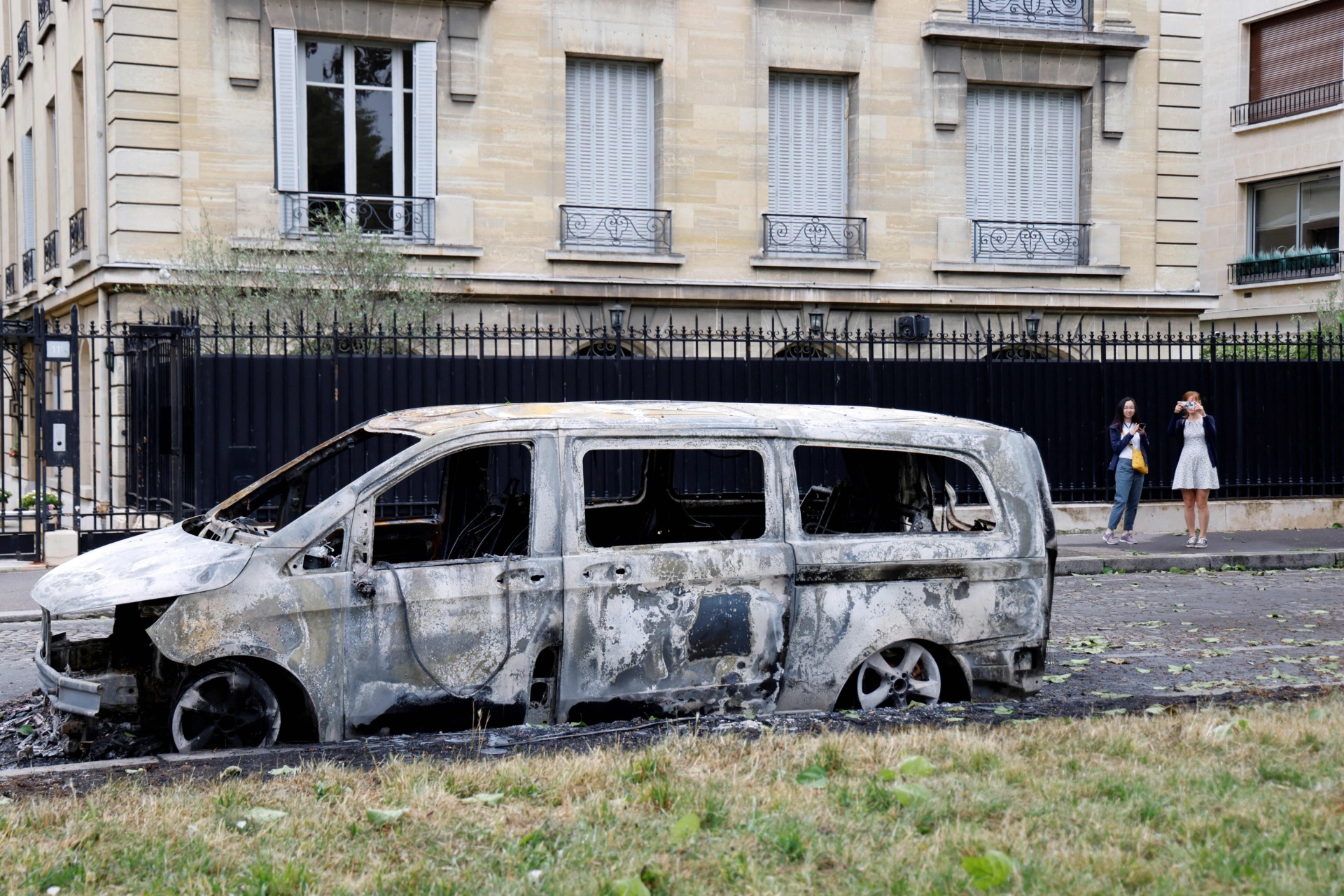 Bystanders take images of a burnt out vehicle in the sixth arrondisement of Paris on July 1, 2023, after continued protests following the shooting of a teenage driver in the suburb of Nanterre on June 27. Violence and looting hit France in a fourth night of protests as massively deployed police made nearly 1,000 arrests and the country braced for more riots ahead of the funeral of the teenager who was killed by an officer during a traffic stop. The government said the violence had "lessened" compared to previous nights, but the interior ministry still reported 994 arrests nationwide overnight, and 79 injuries among police and gendarmes. (Photo by Ludovic MARIN / AFP) (Photo by LUDOVIC MARIN/AFP via Getty Images)