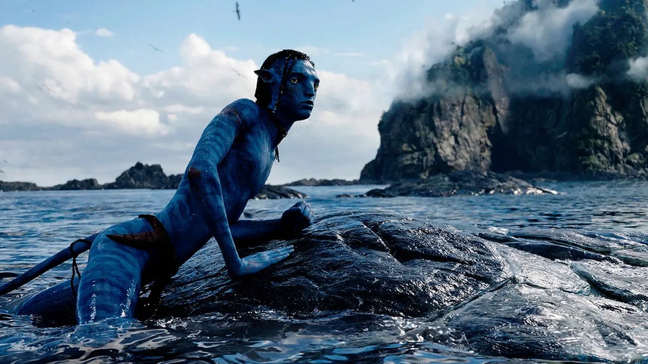 Still from "Avatar: The Way of Water" where an avatar emerges from the water and lays on a rock