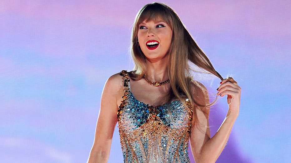 Taylor Swift holds a strand of her hair while looking to the side on stage at the Eras Tour