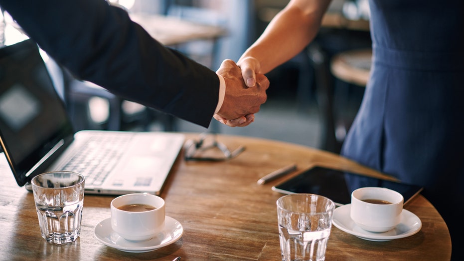 Man and woman shake hands over coffee.