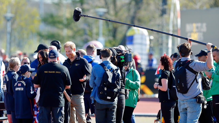 A crew filming Prince Harry and several people waiting to meet him outside