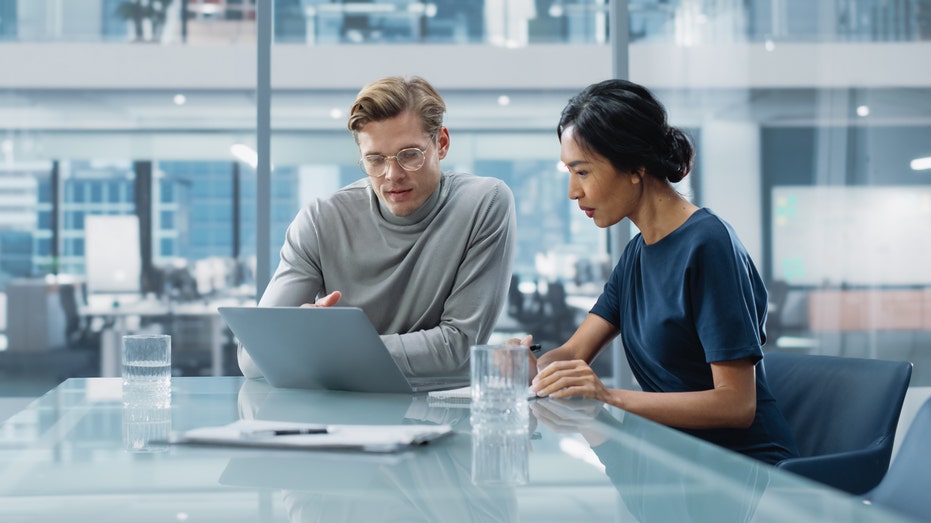 two people sitting and looking at a laptop