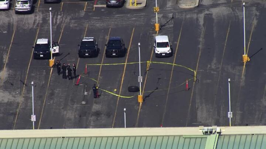 Police cars in parking lot, yellow tape and officers around tape